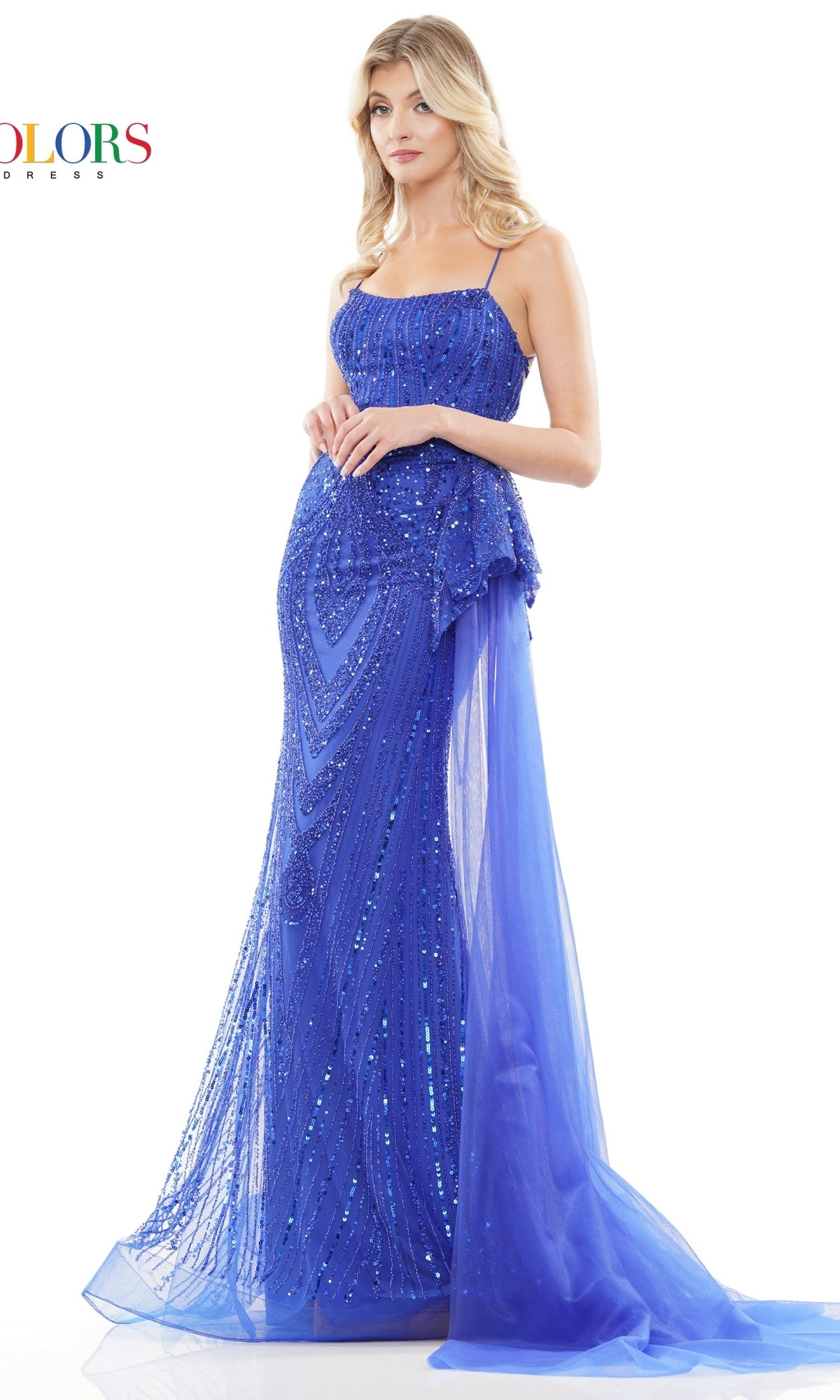 A woman poses against a white background wearing the Lace-Up Beaded Long Prom Dress 3121, a floor-length royal blue gown with thin straps and a sheer overlay.